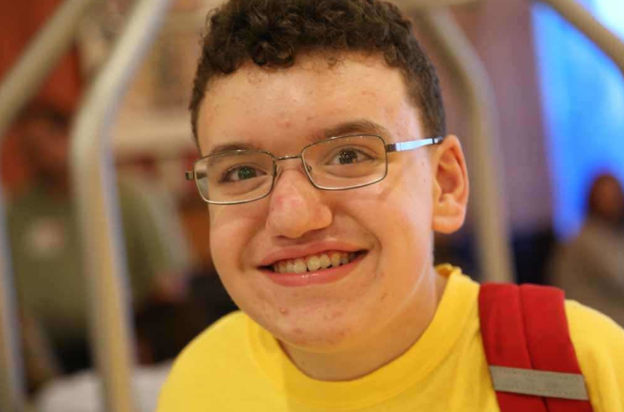 Medical-Management-hero-3 A boy with glasses, brown hair, and a yellow shirt smiles for the camera