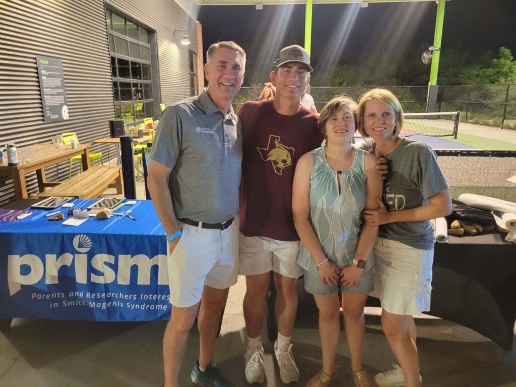 A family poses happily in front of a PRISMS booth at a meetup
